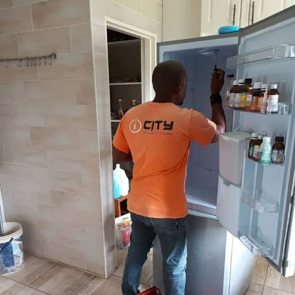 City Appliance Repairs technician working on an open fridge in a customer’s kitchen