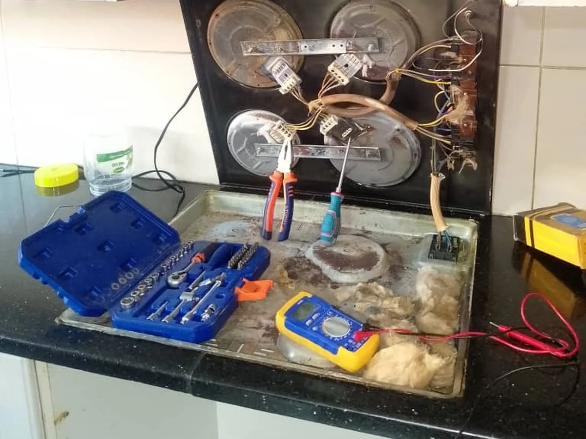 Ceramic hob opened on a kitchen counter with tools and a multimeter during a repair